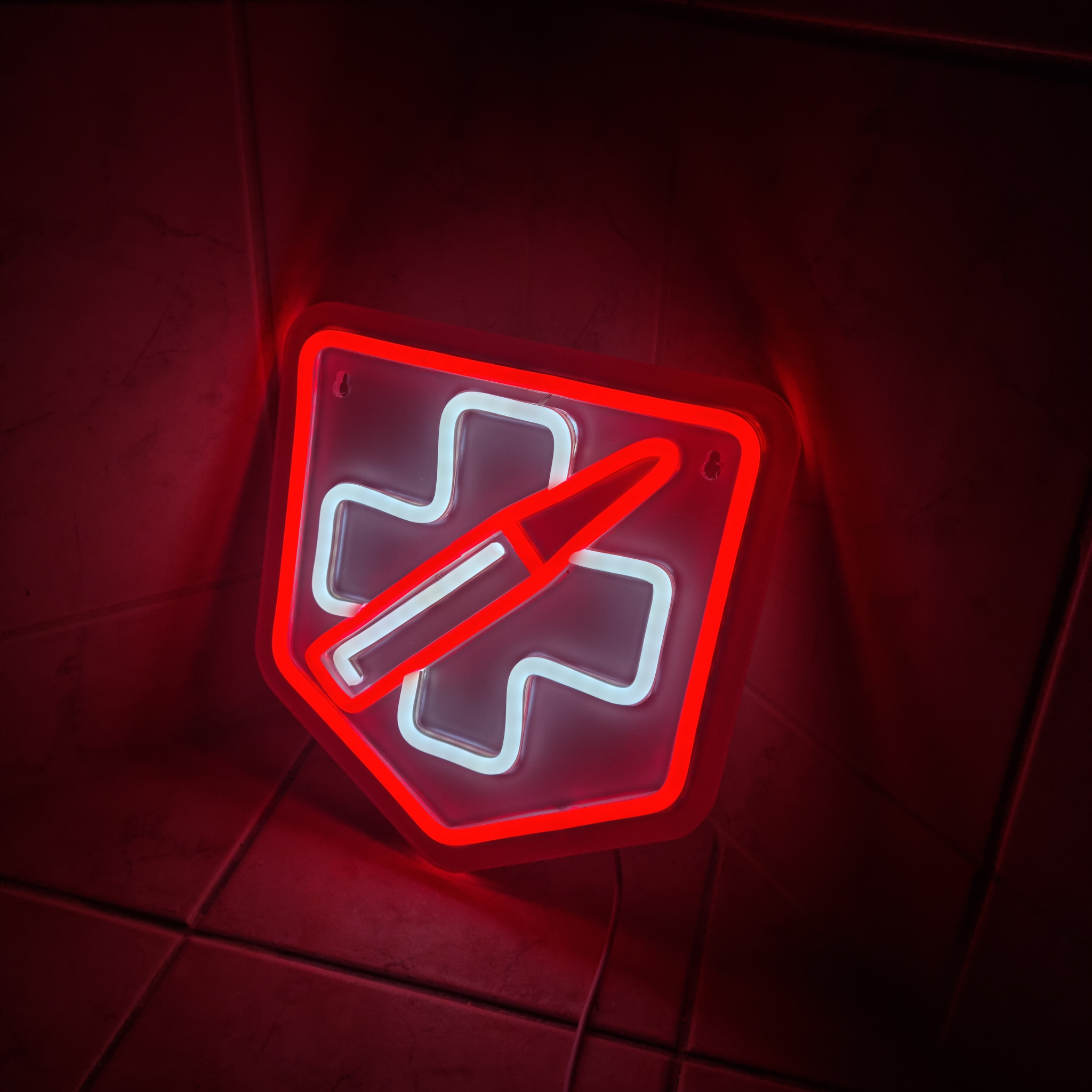 Red and white neon sign of the Call of Duty Zombies Juggernog perk neon sign with a shield with a cross and diagonal slash